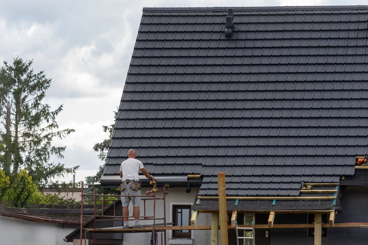 Roofer carefully laying tiles on the pitched roof of a house, working from scaffolding