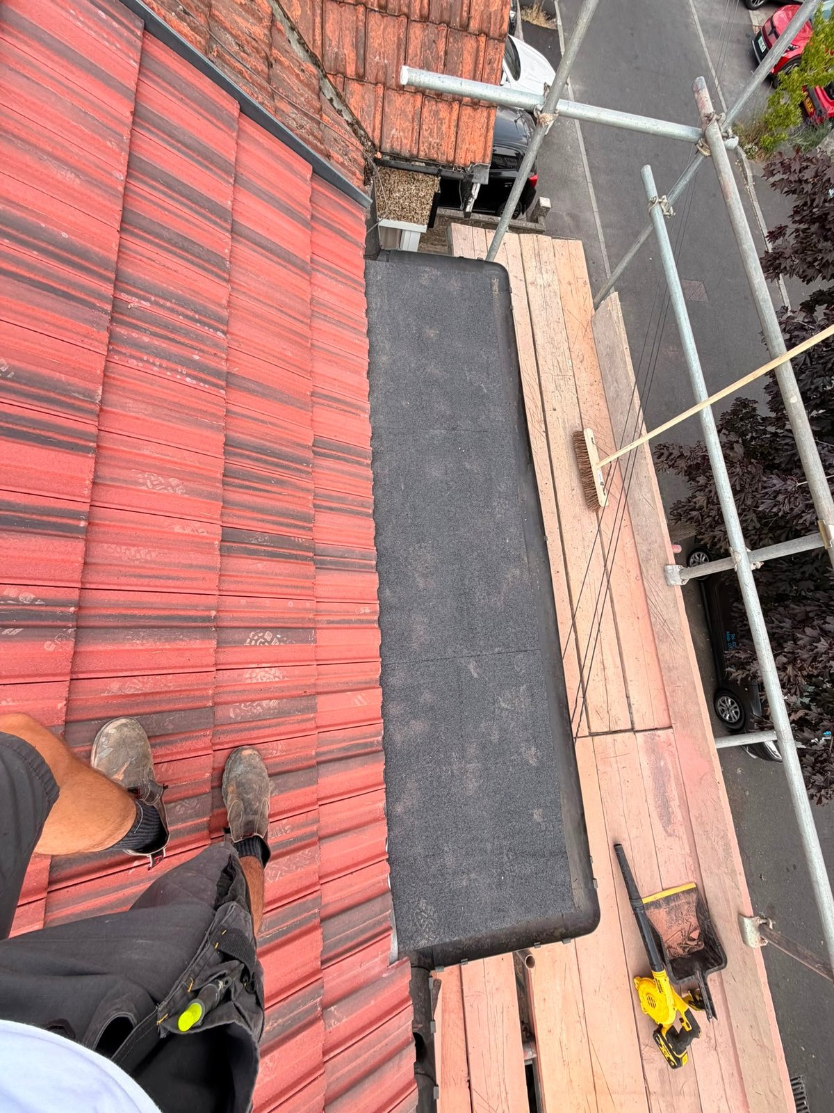 Roofer's-eye view of a red tile roof with new black trim and felt laid, alongside scaffolding boards