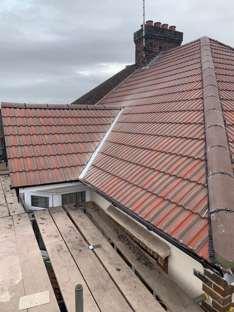 Finished red clay tile roof with chimney stack and walkway boards, viewed from a dormer level