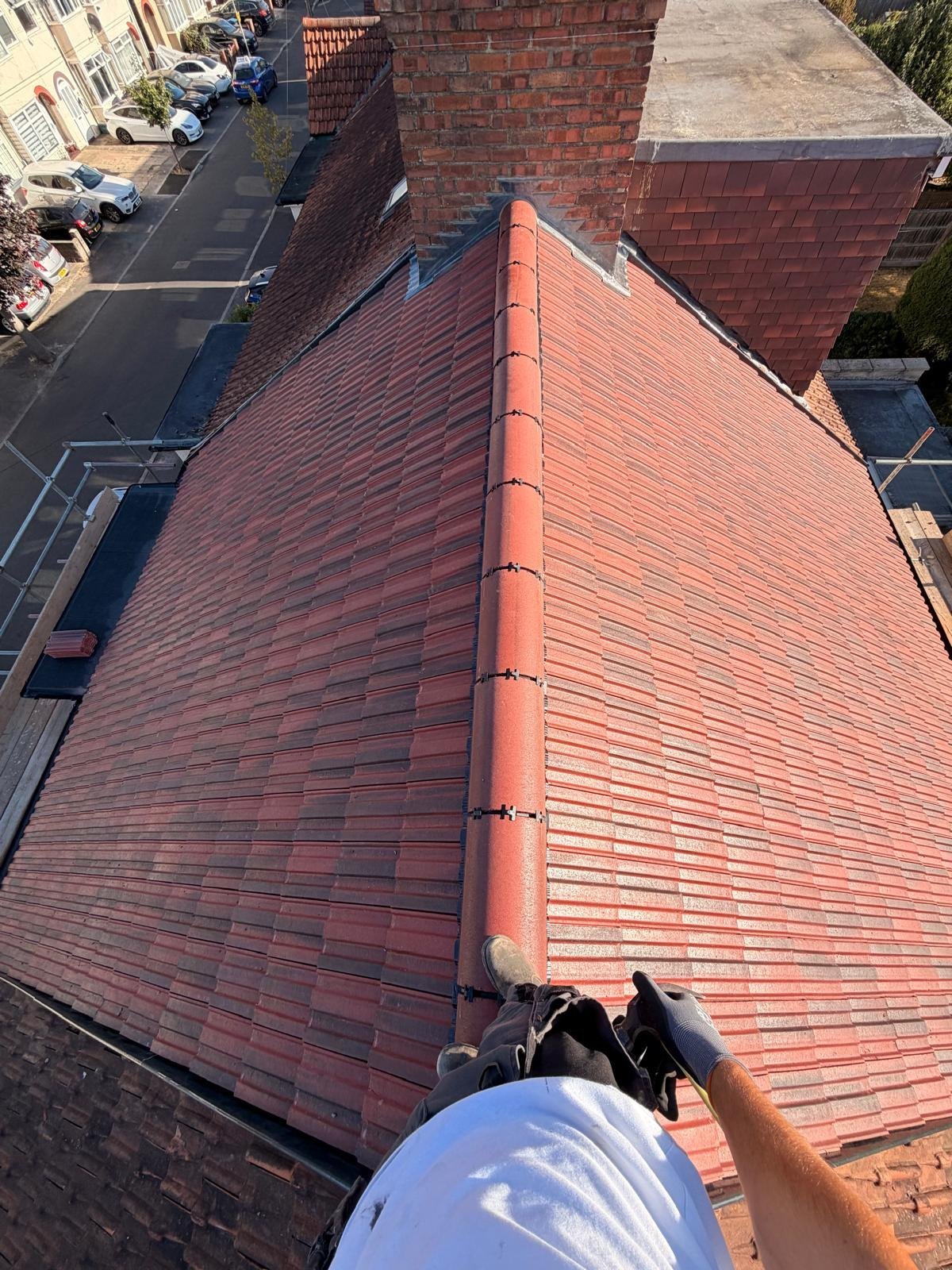 Roofer installing ridge tiles along the apex of a freshly tiled red pitched roof